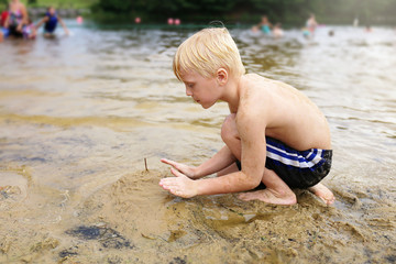 Young Child Playing with Sand on Beach while Swimming in Lake