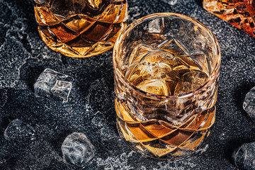 Whiskey with ice on stone dark background.