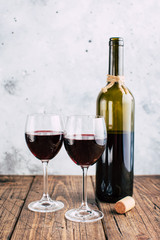 Two glasses of red wine and a bottle, gray stucco background