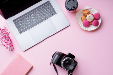 Overhead image of workplace with laptop, coffee, camera and macarons on pink background. Top view, copy space. Creativity concept