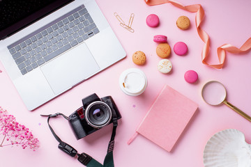 Overhead image of workplace with laptop, coffee, camera and macarons on pink background. Top view,...