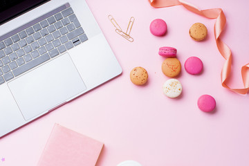 Flatlay with laptop, coffee and macarons on pink background. Top view, copy space. Workplace concept.