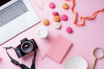Plakat Overhead image of workplace with laptop, coffee, camera and macarons on pink background. Top view, copy space. Creativity concept
