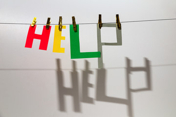 Word "Help" from different color letters is hanging at the rope on the grey background. There are shadow from the letters, clothespins. International Volunteer Day