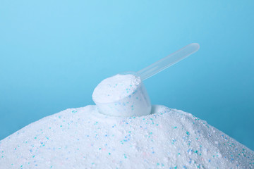 Pile of laundry detergent and measuring scoop against blue background