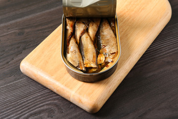 Board with tin can of sprats on wooden table
