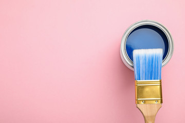 Open can with blue paint and brush on pink background, top view. Space for text
