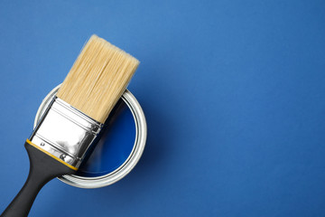 Open can with paint and brush on blue background, top view. Space for text