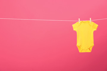 Baby onesie hanging on clothes line against pink background, space for text