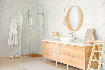 Modern bathroom interior with shower stall, vessel sink and round mirror