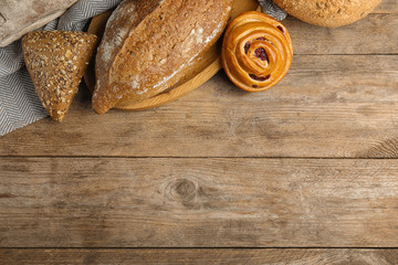 Fresh breads and pastry on wooden background, flat lay. Space for text