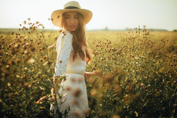 Fototapeta na wymiar Pretty young woman is walking among the flowers on meadow.