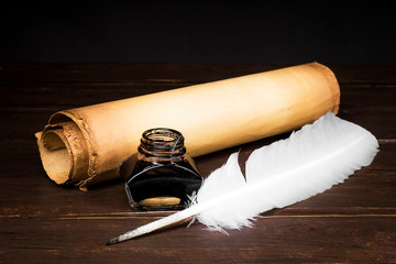 Scrolls of parchment with a pen and inkwell against the background of a table top from boards