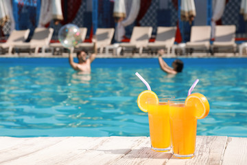 Refreshing cocktails and young couple in swimming pool on background. Space for text