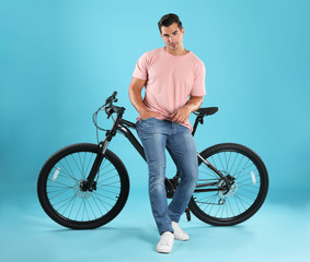 Handsome young man with modern bicycle on light blue background