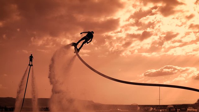 Flyboarding, a new extreme type of activity. Two flyboarders at sunset, fly over a pond. Summer extreme. Silhouettes of athletes against the sky.