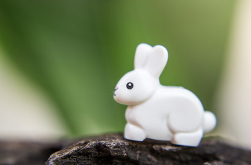 A white rabbit a toy on a stone among grass and flowers