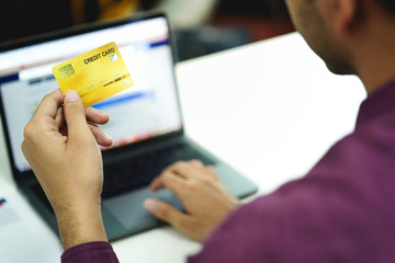 Hand holding credit card, typing on the keyboard of laptop, online shopping and electronic payments concept.  
