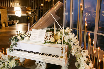 Indoors restaurant during a wedding. Beautiful white piano decorated with natural flowers, candles and a garland.