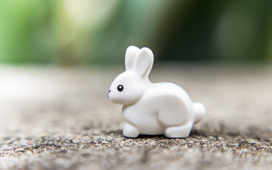 A white rabbit a toy on a stone among grass and flowers