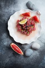 Tuna ceviche with grapefruit juice on a shell-shaped plate, flatlay over grey stone background with pebbles, studio shot