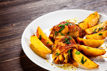 Grilled chicken thighs with baked potatoes on wooden table