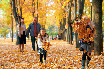 Happy family having holiday in autumn city park. Children and parents posing, smiling, playing and having fun. Bright yellow trees and leaves