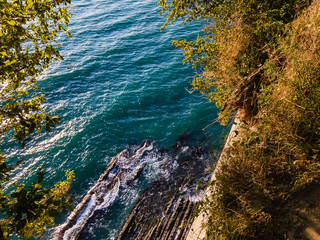 View from the top of the Kiseleva cliff, covered with green vegetation, to the turquoise foam of...