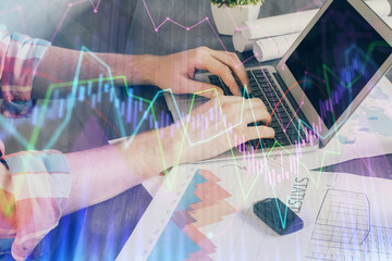 Double exposure of stock graph with businessman typing on computer in office on background. Concept of hard work.