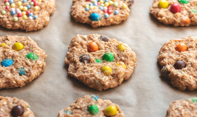Raw cookie dough with colorful chocolate balls on a baking tray close-up.