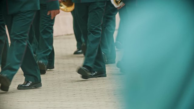 A wind instrument parade - people in green costumes walking on the street holding musical instruments - military musical festival