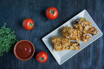 Roasted chicken drumsticks on a plate. Breaded chicken drumsticks, fried chicken. Dark wooden background.