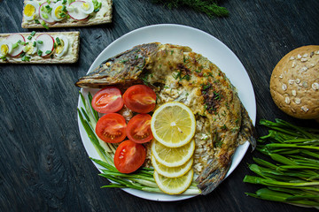 Baked pike in the oven, decorated with vegetables and herbs. Serving on a plate. Proper nutrition. Dark wood background.