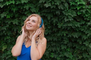 Beautiful young blonde girl in a dress listening to music in blue headphones. Real life, enjoy the moments. Copy space.