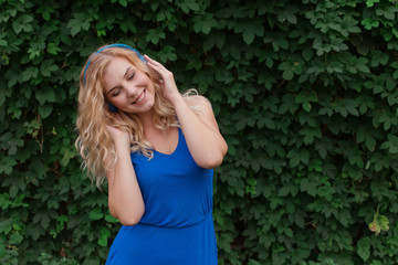 Beautiful young blonde girl in a dress listening to music in blue headphones. Real life, enjoy the moments. Copy space.