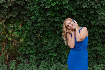 Beautiful young blonde girl in a dress listening to music in blue headphones. Real life, enjoy the moments. Copy space.