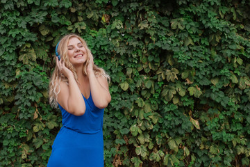 Beautiful young blonde girl in a dress listening to music in blue headphones. Real life, enjoy the moments. Copy space.