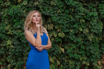 Young beautiful girl on a background of a wall of wild grapes, ponders, thinks an idea. Copy space.