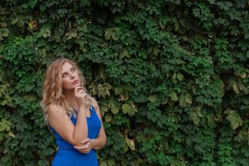 Young beautiful girl on a background of a wall of wild grapes, ponders, thinks an idea. Copy space.