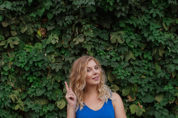 Young beautiful girl on a background of a wall of wild grapes, ponders, thinks an idea. Copy space.