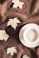 Autumn home cozy composition. Cup of coffee, knitted plaid, dried autumn leaves on brown background. Fall background. Flat lay, top view, copy space
