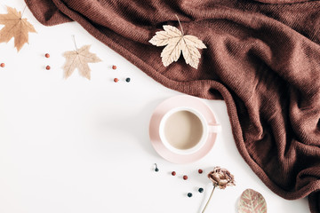 Autumn home cozy composition. Cup of coffee, knitted plaid, dried autumn leaves, berries, flowers on white background. Fall background. Flat lay, top view, copy space