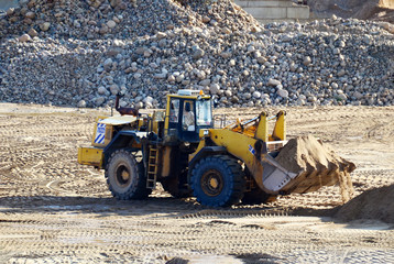 Large heavy front-end loader or all-wheel bulldozer for mechanization of loading, digging and excavation operations in open quarry. Crusher plant with belt conveyor, crushing process, grinding stone