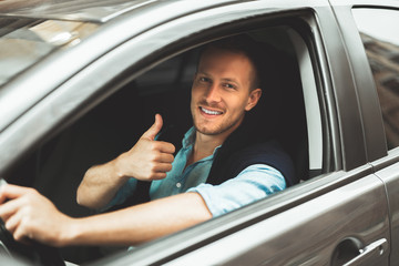 young handsome man driving car close up showing ok sign