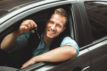 young handsome man feels happy holding car keys sitting in his new car