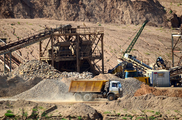 View on the mining quarry for the production of crushed stone, sand and gravel. Crusher plant with belt conveyor, crushing process, grinding stone. Dump trucks transporting sand in the open-pit.