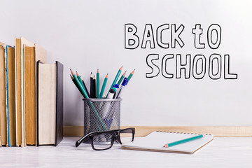 The inscription marker on a white board, Back to School. A table with books and glasses attributes for writing.