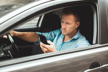 young handsome man drives unsafely checking his smartphone on the run
