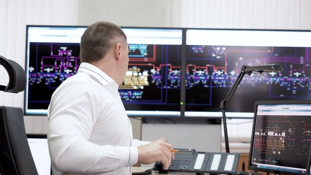 Manager Calling Phone And Making Paper Work. Man Office Worker Operator Working In Control Center Room Of Electric Power Station Using Digital Screens With Schemes. Power And Energy Industry Plant.