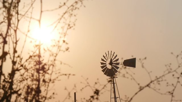 A windpump windmill spinning against a golden glowing sunset